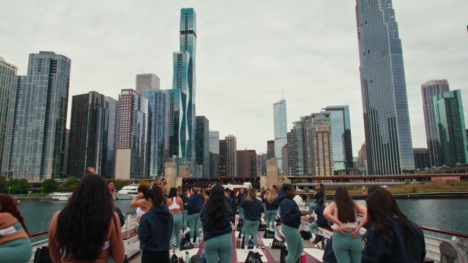 Guests in matching Pilates sets on the deck of a boat on the Chicago River, with the skyline ahead